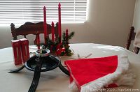 Photo showing black metal Christmas tree stand, red candle centerpiece, two boxed red candle replacements, and red and white Christmas tree skirt.