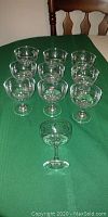 10 desert glasses arranged in pyramid formation on green tablecloth, clear glass with etched floral patterns visible.