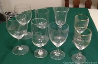 Nine assorted wine glasses on a green tablecloth, including variations in bowl shape and size, some with gold rims.