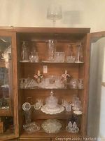 Glass cabinet displaying a large variety of cut glassware including bowls, trays, candy dishes, salt and pepper shakers, and glasses