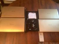 Four gold presentation boxes on table and one open box showing purple crystal tassel necklace and slide ring