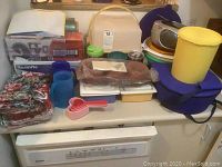 Overview of assorted kitchen items including Pyrex covered dish with carrying case, plastic containers, measuring spoons, and floral fabric items.