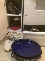 Various bakeware pans and kitchen utensils stored on floor and shelves in kitchen area
