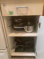 Shelves cupboard showing stacked sauce pans, skillets, and one stainless steel saucepan with lid