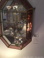 Front view of one octagonal wall-mounted glass display cabinet showing multiple Swarovski crystal figurines on glass shelves