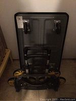 Photo of black folding rolling cart with label and wheels visible, folded state