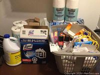 Photo of cleaning supplies including Lysol toilet cleaner 4 pack, bleach jug, Kirkland paper towel rolls, and basket with various smaller cleaning products.