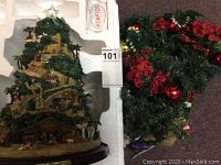 Full view of the Thomas Kinkade Nativity Tree in white foam packaging next to decorated Christmas wreath.