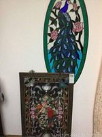 Both stained glass wall hangings displayed on wall; oval peacock piece behind rectangular parrots piece