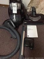 Assembly of Kenmore AllFloors canister vacuum with hose, wand, vacuum head, additional attachment and manual laid out on carpeted floor.
