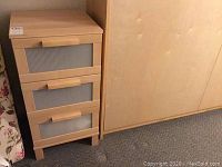 Full view of the night stand against a wall, showing 3 drawers and wooden handles.
