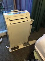 White Uberhaus portable air conditioner with control panel on top, remote placed on unit, vent extension piece in front.