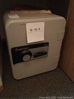 Full view of the Sentry safe, gray color, with combination dial lock, placed on a carpeted floor.