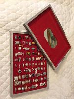 Overhead view of open silver-tone hinged box showing full tray of rings against red velvet interior