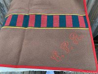 Brown fleece blanket with red and dark green vertical stripes bordered by yellow lines. Red edging and embroidered red 'C.P.R.' lettering visible.