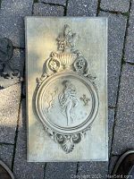 Top view of rectangular stone plaque with classical female figure relief, showing ornate floral and vase decorations.