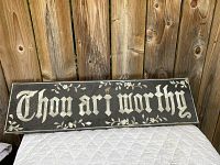 Front view of antique 'Thou Art Worthy' sign with mother of pearl letters on dark background.