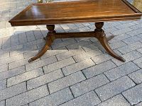 Full view of the antique wooden coffee table showing the rectangular tabletop and pedestal legs on brick patio.