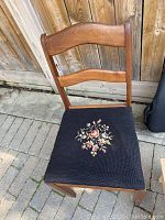 Front view of wooden chair with black needlepoint seat showing floral embroidery in excellent condition