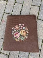 Front view of square antique needlepoint chair seat cushion with floral embroidery on brown background.
