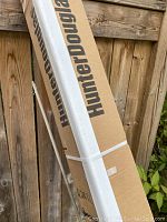 Packed boxes of Hunter Douglas window shades with brand label visible, leaning against wooden fence outdoors.