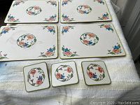 Top view of four rectangular placemats and three square coasters laid out on a cloth surface showing floral design front side
