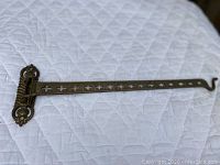 Full length view of the antique brass swing arm with hook showing the decorative cut-out design and aged brass patina.