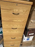 Front view of the oak filing cabinet showing four drawers with black handles and a lock on the top drawer, showcasing wood grain finish and condition.