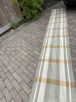 Full length of the handwoven fabric runner showing its plaid pattern and color scheme, laid out on a paved driveway.