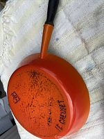 Bottom view of orange Le Creuset frying pan showing brand and signs of wear