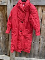 Full red women's down coat hanging on wooden fence showing overall condition and style.