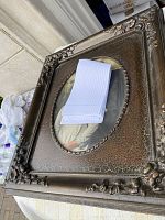 Front view of a vintage ornate picture frame with oval opening and a folded white cloth inside.