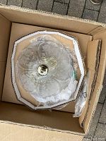 Top view of the crystal glass fixture in packaging showing floral etched patterns and central brass fitting.