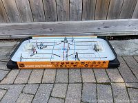 Full view of the Power Play tabletop hockey game showing the playing surface, player figures, goals, and orange side panels with hockey logos.