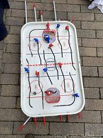 Top-down view of the hockey game showing the red and blue player figures positioned on rods with the puck on the ice rink playing surface.