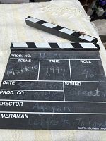 Front view of the vintage wooden film clapperboard with handwritten chalk details showing scene, take, roll, and production information.