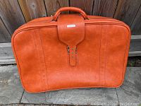 Front view of the orange Samsonite suitcase on stone patio, showing front buckle closure and handle.