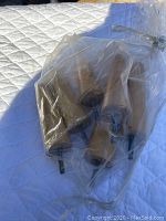 Six tapered wooden furniture legs inside a clear plastic bag, showing metal screw inserts at the top, displayed on a white quilted surface outdoors in sunlight.