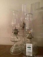 Three clear glass hurricane lamps arranged together showing varying heights and metal wick holders beneath clear glass chimneys.