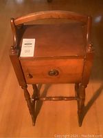 Front view showing top surface, cupboard door with decorative circular wood detail and knob handle, and turned legs