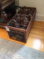 Wide shot of vintage wooden crate filled with large pine cones on hardwood floor near rug and furniture.