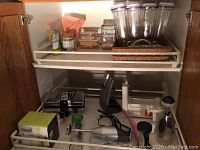 KitchenAid hand mixer, slow cooker, various kitchen utensils and spice containers inside a cabinet.
