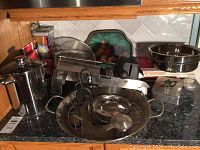Full view of the kitchen countertop showing mandoline, knife block, stainless steel pans, steamers, and strainers.