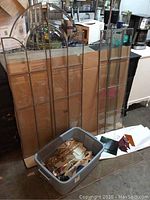 Two large lead framed clear glass panels leaning against a cardboard backing with a plastic bin of stained glass pieces in front.