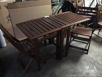 Wooden patio table with drop sides and folding chairs in a garage setting, showing table surface and side views.