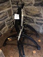Photo showing the full bike rack with three metal support arms and straps for securing bike tires, set against stone wall background.