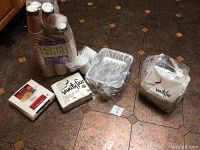Photo showing Vanity Fair napkins in two unopened packs, disposable aluminum casserole containers stacked, and a large opened package of disposable hot/cold cups with lids.