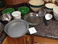 Various pottery and metal mixing bowls, loaf pans, Teflon cake pans, glass pie plates arranged on a kitchen counter.