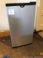 Full view of the Oster mini refrigerator showing silver exterior and black top.