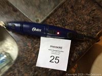 Oster nail grinder electric tool with metal grinding bit attached, plugged in and powered on, resting on dark surface